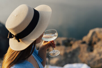 Woman in straw summer hat  tasting wine at nature. She enjoying beautiful landscape while drinking...