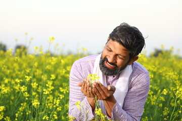 Happy Indian farmer admiring a flower of his field while bending towards the level of of the flower.