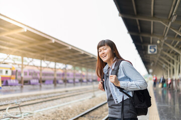 Asian woman waiting the train at train station for travel. Backpack traveler using generic local map sitting alone at train station platform. Tourist adventure holiday traveling concept.