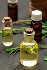 Natural rosemary essential oil in a glass bottle and a fresh sprig of rosemary on a black background. face and body skin care. spa.