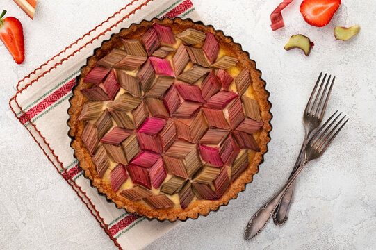 Rhubarb custard tart with geometric pattern and strawberry jam on a light stone table. Spring and summer sweet-sour healthy dessert. Top view