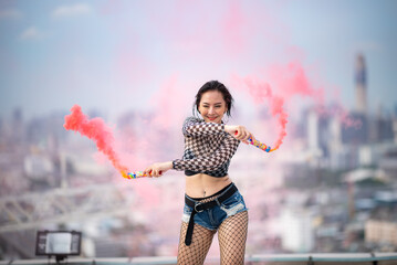 Fototapeta na wymiar Beautiful Asian female hip hop dancer striking a sexy dance pose, attractive sexy dancer women dancing with colored smoke bomb on rooftop with skyscraper city view, hip hop street dance