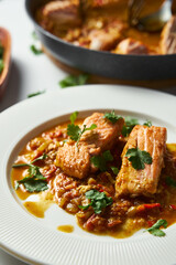 Indian red salmon curry with tomatoes. Asian Cuisine. Fried salmon with vegetables and green cilantro in white plate. Close up. Vertical photo 