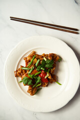 Chicken Manchurian on white plate with chopsticks. White marble background. Sweet and sour Chinese chicken recipe 