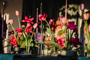 Festive dinner table is served dishes and cutlery and decorated with flowers tulips and greenery, candles. Birthday celebration. Family holidays in modern dining room. Stylish spring party. Wedding.