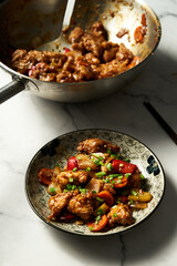 Chicken Manchurian in plate near wok where chicken was fried and cooked with sauce. 