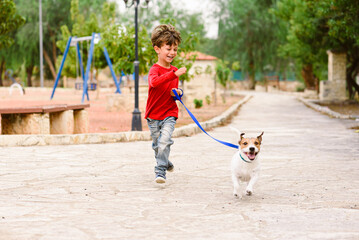 Happy smiling small boy playing and running with his pet dog in park