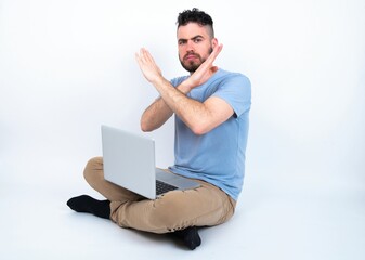 Young caucasian man with laptop sitting over white studio Rejection expression crossing arms doing negative sign, angry face