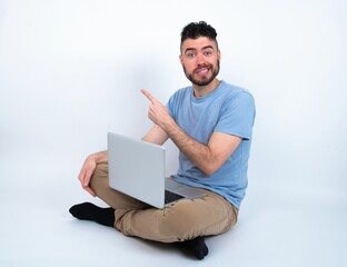 Young caucasian man with laptop sitting over white studio Pointing aside worried and nervous with forefinger, concern and surprise concept.