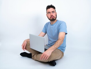 Young caucasian man with laptop sitting over white studio making grimace and crazy face, screaming out of control, funny lunatic expressing freedom and wild.