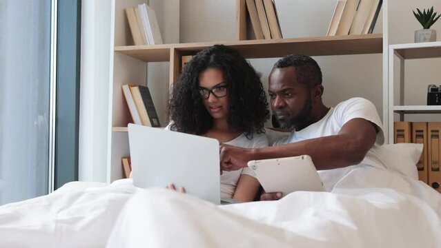 Cheerful amorous people accessing portable computer while spending time together in spacious apartment at weekend. Joyful multiethnic family scrolling social media on wireless laptop.