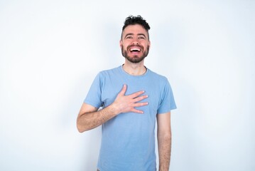 Fototapeta premium Young caucasian man wearing blue T-shirt over white background smiles toothily cannot believe eyes expresses good emotions and surprisement