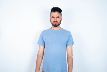 Offended dissatisfied Young caucasian man wearing blue T-shirt over white background with moody displeased expression at camera being disappointed by something