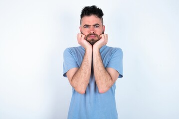 Portrait of sad Young caucasian man wearing blue T-shirt over white background hands face