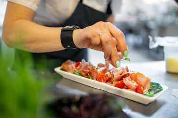 Chef decorate ready dish with slices parma ham on restaurant kitchen