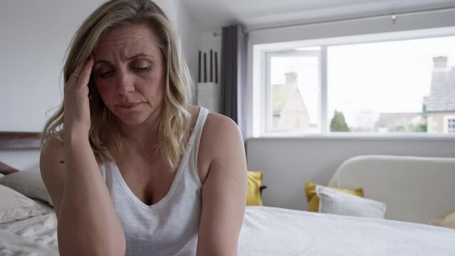Menopausal Mature Woman Suffering With Low Mood And Anxiety Sitting On Bed At Home 