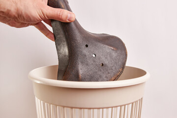 An old bicycle saddle is thrown into the trash can. Waste disposal and recycling.