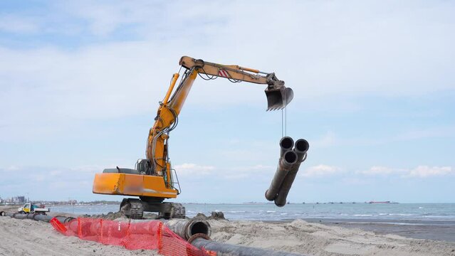Orange tracked excavator carries three pipes on the sea