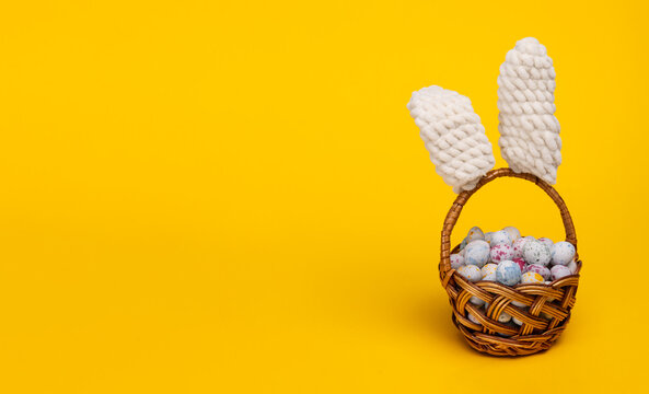Easter greeting card. colored easter eggs in a basket with bunny ears on a yellow background with copy space