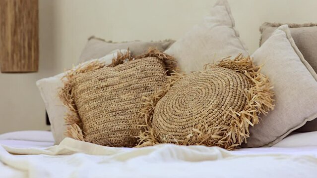 Close-up of beautiful straw handmade boho style pillows on messy bed in exotic Bali villa