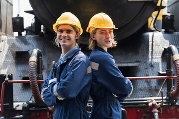 Male and female engineer workers working in locomotive garage, standing with crossed arms, wearing safety uniform and helmet. Group of technician worker at work in locomotive garage workshop