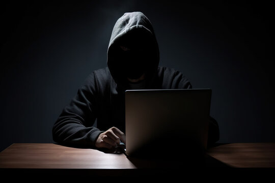 Hacker wearing black hoodie using laptop computer while working on dark background. Created with Generative AI Technology