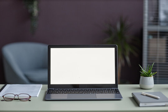 Background image of open laptop with white screen mockup on desk in elegant office setting decorated with plants