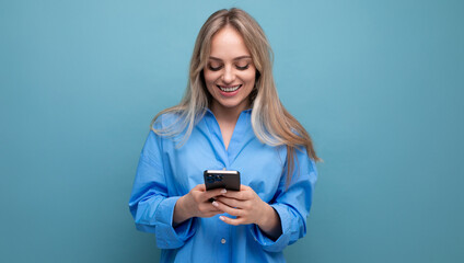 Fototapeta premium joyful charming blonde woman chatting in a smartphone application on a blue bright background