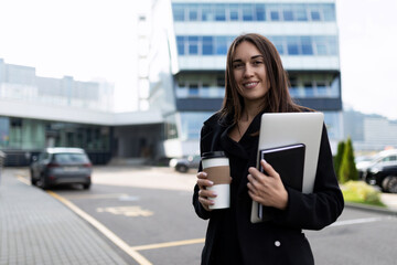 businesswoman with a laptop and documents in her hands against the backdrop of a city business building