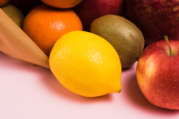 Fruits in a reusable bag on a pink background, lemon and apple close-up. Earth day and zero waste concept.