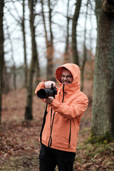 A young and smiling male while taking photos of the forest around him. Progressive photographer with a modern and expensive mirrorless camera. A man holding a camera with a telezoom lens in his hands.