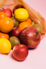 Fruits in a reusable bag on a pink background, pomegranate fruit, kiwi, lemon and apple close-up. Earth day and zero waste concept.