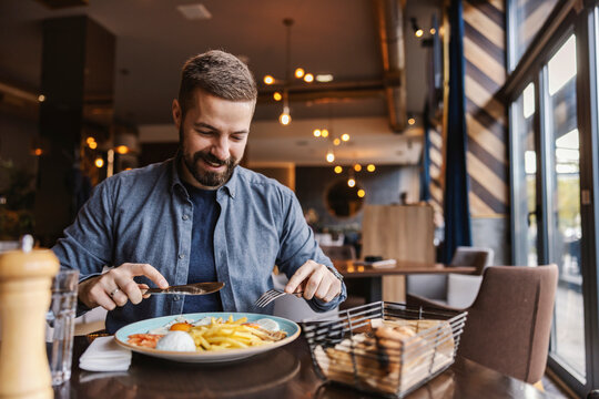 A Hungry Young Man Is Sitting In A Restaurant And Having Eggs For Breakfast.