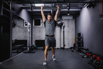 Fototapeta na wymiar Confidence and powerful movement, commitment to sports. Strong man in sportswear does an exercise, lifting weights in a modern gym concept. Healthy lifestyle, stay in good shape, sports life