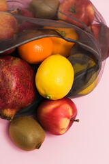 Fruits in a gray transparent reusable bag on a pink paper background. Earth day and zero waste concept.