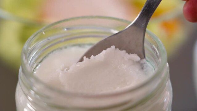 Spooning coconut oil in a glass jar for cooking dietary food. Close up