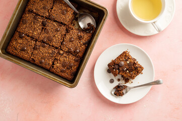 Close up brownies with chocolate chips and rolled oats served with cup of tea on pink background
