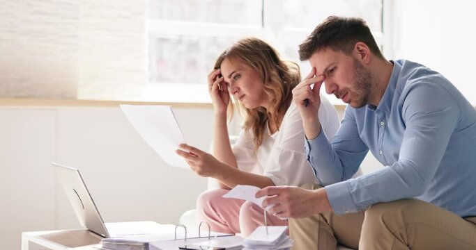 Shocked Young Couple Sitting On Sofa Looking At Bill