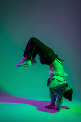 Obraz premium Fashion handsome hip hop dancer man b-boy in trendy denim clothes dancing in motion and standing on his hands in a creative color studio with green and purple light