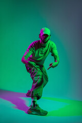 Fototapeta na wymiar Cool fashion professional artist dancer man model with cap in stylish clothes with fashionable sneakers dancing and posing in creative color studio with green and pink light
