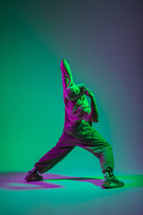 Fototapeta na wymiar Stylish professional dancer man with a cap in trendy fashion clothes dancing in a colorful creative studio with cyan and pink lights