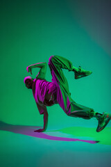 Obraz na płótnie Canvas Stylish professional dancer guy hip hop b-boy in fashionable clothes with a cap and sneakers dances on hand in a creative studio with magenta and cyan color