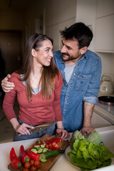 Lovely young couple looking at each other lovingly while making a meal together.