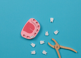 Toy wooden dentist set. Toy jaw with teeth and dentist forceps. Top view on a blue background.