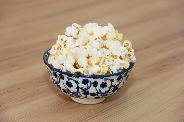 White fried popcorn in a decorative plate on a brown background