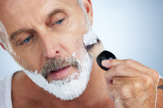 Man, beard and shaving cream for grooming, skincare or hair removal against a studio background. Closeup of male face applying shave creme or foam product with brush for haircare or facial treatment