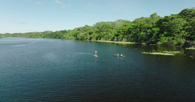 Aerial: Drone Forward Shot Of People Rowing And Paddleboarding On Rippled River By Green Trees In Forest During Vacation - Peruvian Amazonia, Peru