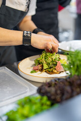 chef hand cooking Roast beef salad with vegetables on restaurant kitchen