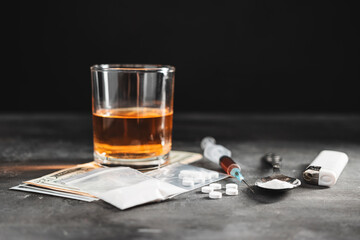 Alcohol drink in a glass, syringe with a dose of drugs, white pills in a transparent bag, narcotics powder in a spoon and US dollar cash on dark background. Concept of addiction and bad habits