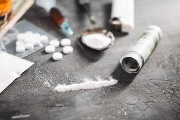 Line of white powder narcotics, white pills, syringe with a dose of drugs and rolled US dollar banknote on dark background. Concept of addiction and bad habits